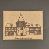 Kraft paper card with a printed illustration of a half-timbered house and text on a gray background